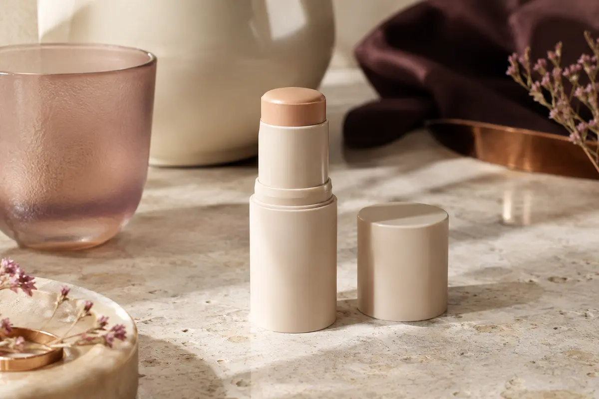Stick solaire mat compact posé sur une surface de pierre claire, près d’un verre dépoli et d’une coupelle ivoire.