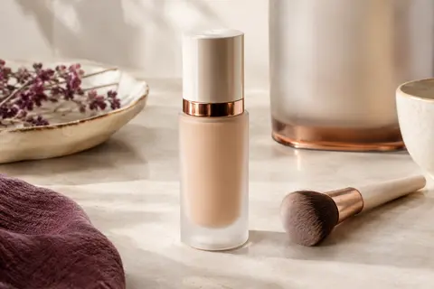 Flacon de fond de teint liquide beige clair posé sur une pierre claire dans un décor de beauté épuré