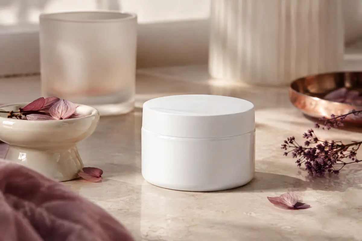 Baume hydratant pour le visage et le corps posé sur une pierre claire avec des accessoires ivoire