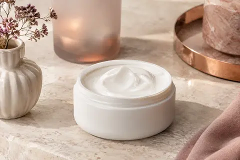 Crème hydratante lissante dans un contenant blanc neutre, posée sur une pierre claire.