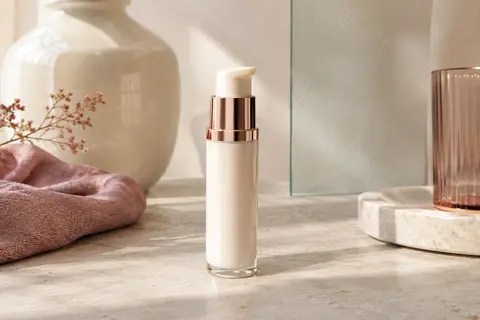 Crème hydratante visage en tube-pompe posée sur une pierre claire avec du verre dépoli et de la céramique ivoire