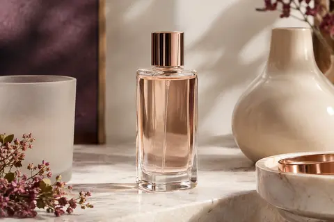 Flacon élancé d’eau de parfum présenté sur une surface de pierre claire, dans une lumière douce.