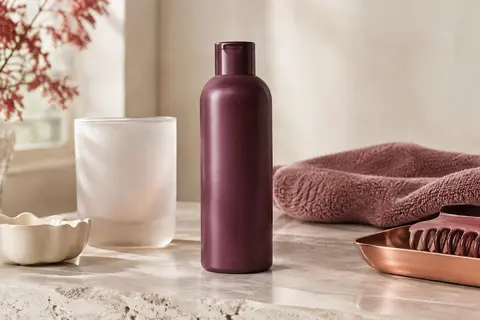 Flacon neutre de shampoing pour cheveux colorés posé sur une pierre claire, près de verre dépoli