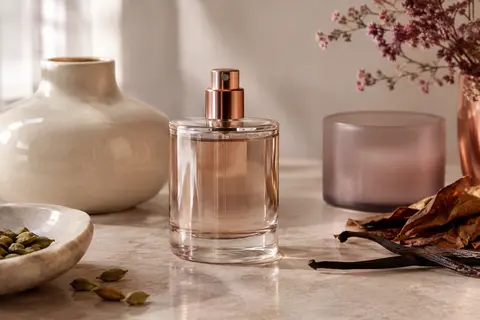 Flacon d’eau de toilette posé sur pierre claire, avec céramique ivoire et reflets doux.