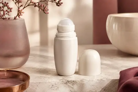 Flacon roll-on de déodorant anti-transpirant posé sur une pierre claire près d’un verre dépoli