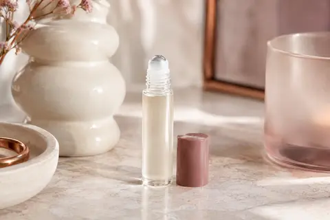 Flacon roll-on détranspirant posé sur une pierre claire, près d’un verre dépoli et d’une céramique ivoire.