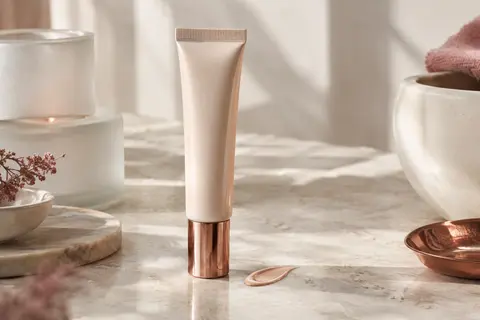 Tube de fluide solaire visage teinté posé sur une pierre claire près d’une touche de texture lumineuse.