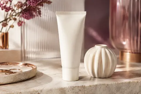 Tube de crème visage Illiyoon posé sur une pierre claire, près d’un flacon en verre dépoli et d’une céramique ivoire.