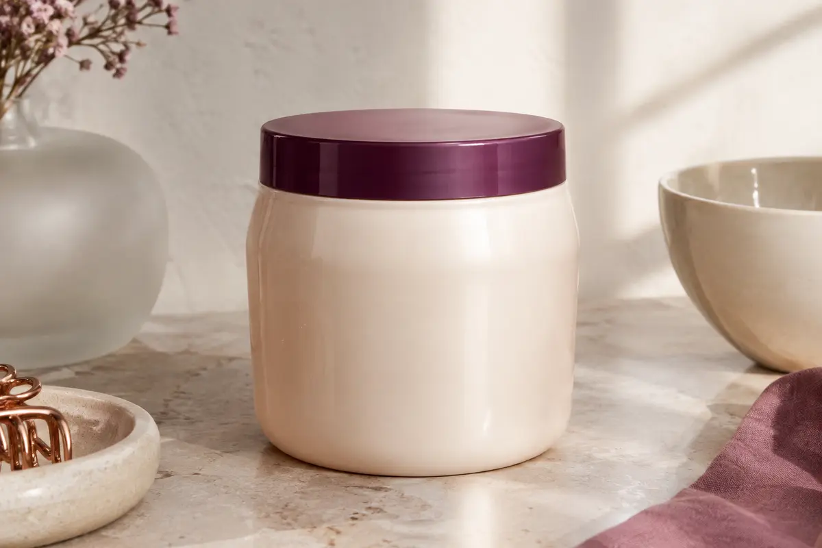 Bouteille de masque capillaire posée sur une pierre claire près d’un verre dépoli et d’une céramique ivoire.