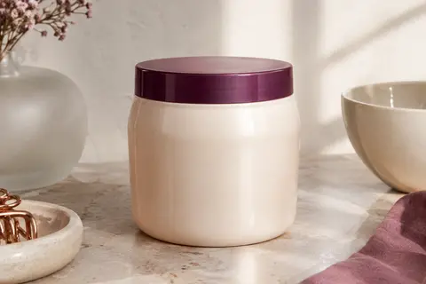 Bouteille de masque capillaire posée sur une pierre claire près d’un verre dépoli et d’une céramique ivoire.