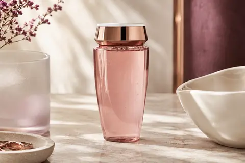 Flacon de shampooing liquide Genesis posé sur une pierre claire près d’un verre dépoli et d’une coupelle ivoire.