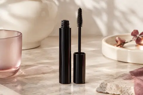 Tube de mascara avec brosse à picots multi-niveaux et trace de formule noire sur une pierre claire