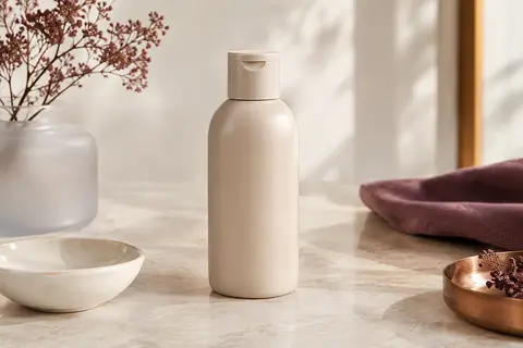Flacon de shampooing Metal Detox posé sur une pierre claire, avec du verre dépoli et de la céramique ivoire