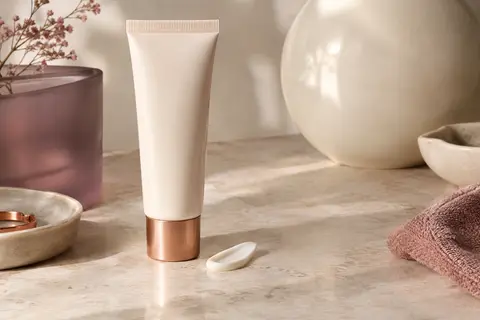 Deux tubes de crème solaire visage présentés sur une pierre claire avec du verre dépoli et une coupelle ivoire.