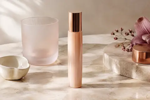 Fluide solaire visage dans un contenant compact posé sur une pierre claire près d’un verre dépoli.
