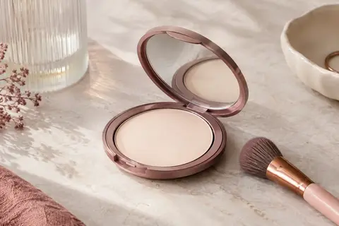 Poudre compacte cuite beige clair présentée dans un boîtier ouvert sur une pierre claire