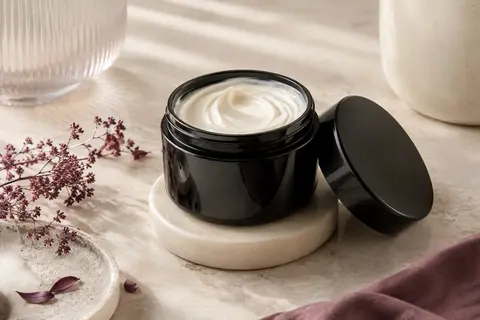 Pot sombre ouvert de masque capillaire crémeux présenté sur une surface claire avec une coupelle ivoire