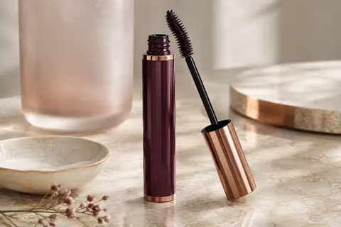 Tube de mascara et brosse incurvée aux nombreux poils posés sur une pierre claire