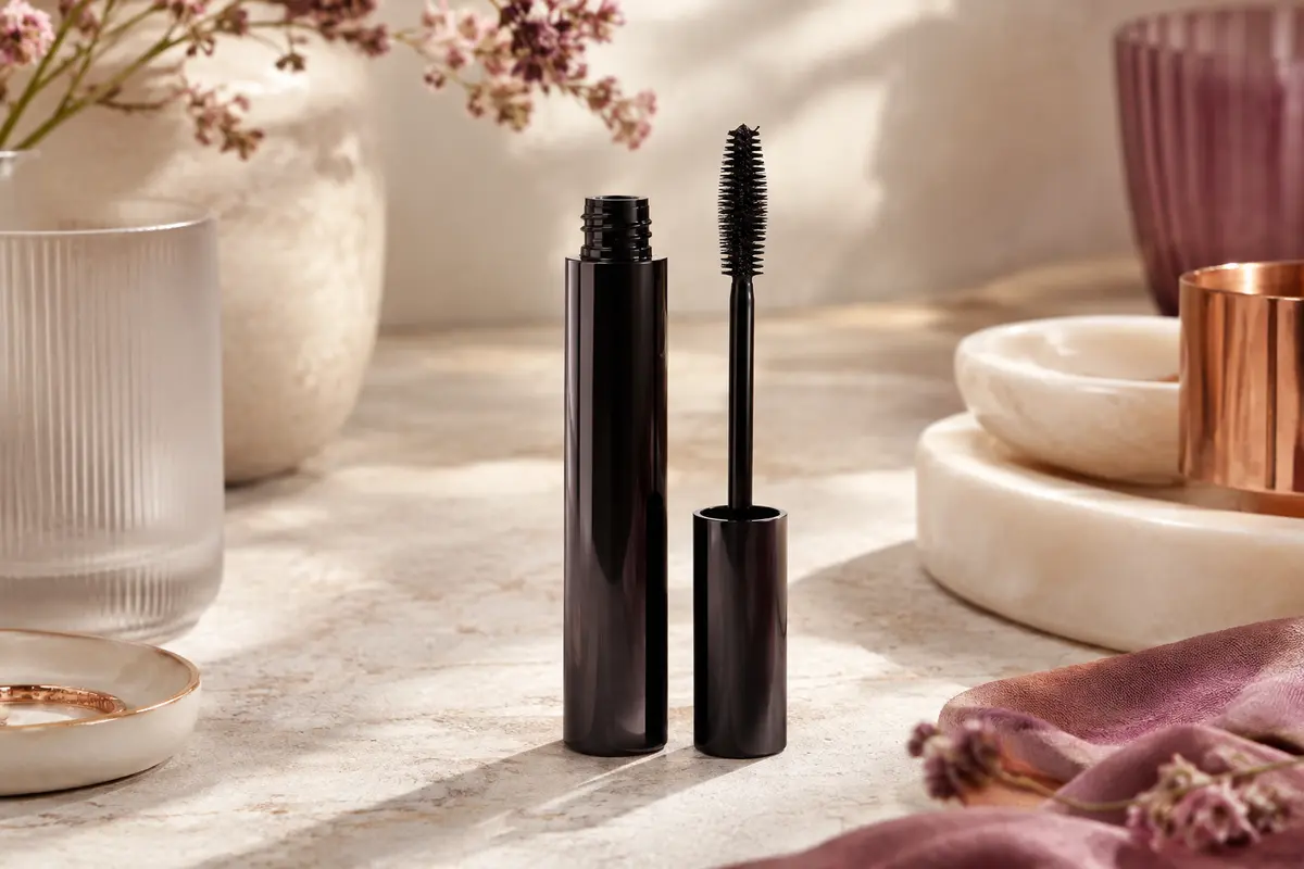 Tube de mascara volumateur ouvert, avec sa brosse Millionizer noire posée sur une pierre claire.