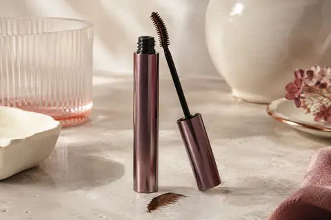 Tube de mascara marron et brosse incurvée présentés sur une surface en pierre claire