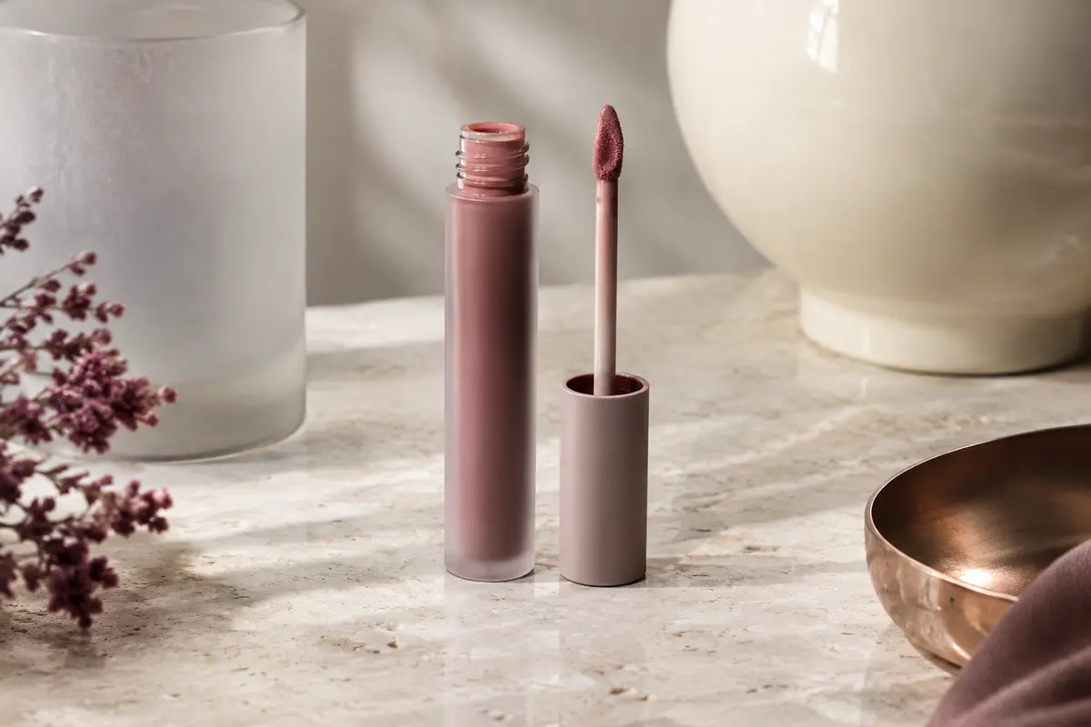 Rouge à lèvres liquide nude froid au fini mat, avec son applicateur de précision sur une pierre claire.