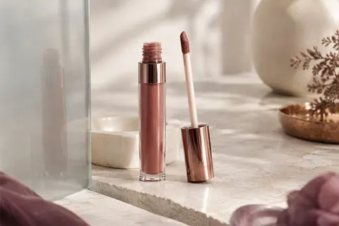 Rouge à lèvres liquide mat en tube avec applicateur flèche, posé sur une pierre claire près d’une céramique ivoire.