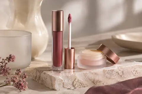 Duo de rouge à lèvres liquide rose et baume confort posé sur une surface en pierre claire