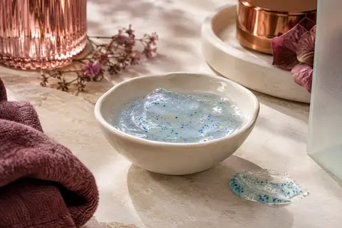 Gel nettoyant visage aux capsules bleues présenté sur une pierre claire avec une coupelle ivoire.