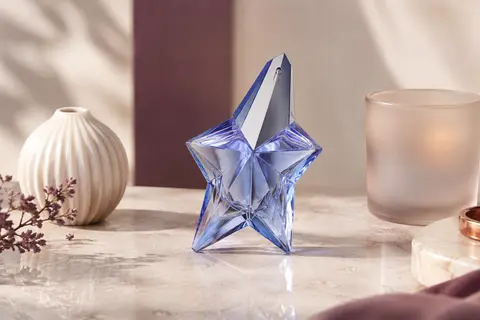 Flacon vaporisateur de l’eau de parfum Mugler Angel posé sur une surface de pierre claire