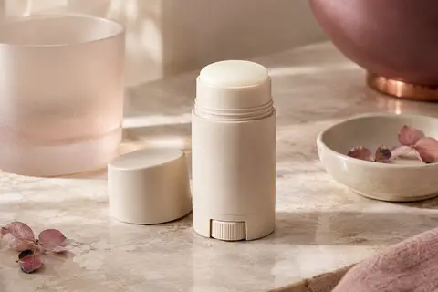 Stick déodorant anti-transpirant compact posé sur une pierre claire près d’un flacon en verre dépoli.