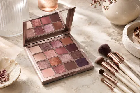 Palette de maquillage ouverte aux nombreuses poudres colorées, accompagnée de pinceaux sur une pierre claire
