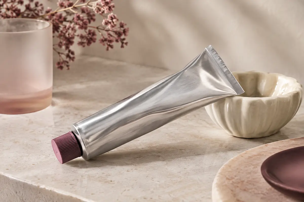 Tube de crème nourrissante en aluminium posé sur une pierre claire avec une touche de texture riche