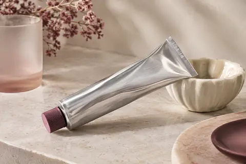 Tube de crème nourrissante en aluminium posé sur une pierre claire avec une touche de texture riche