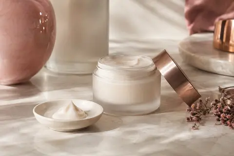 Crème visage et corps Weleda Skin Food mise en scène sur pierre claire avec des fleurs et une coupelle ivoire