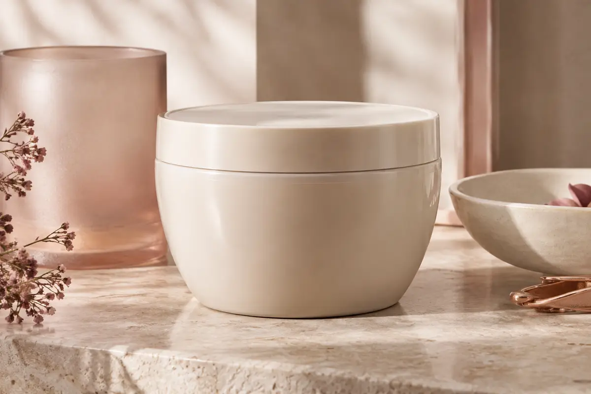 Masque capillaire nourrissant présenté sur une pierre claire avec une texture crémeuse et des accessoires ivoire.